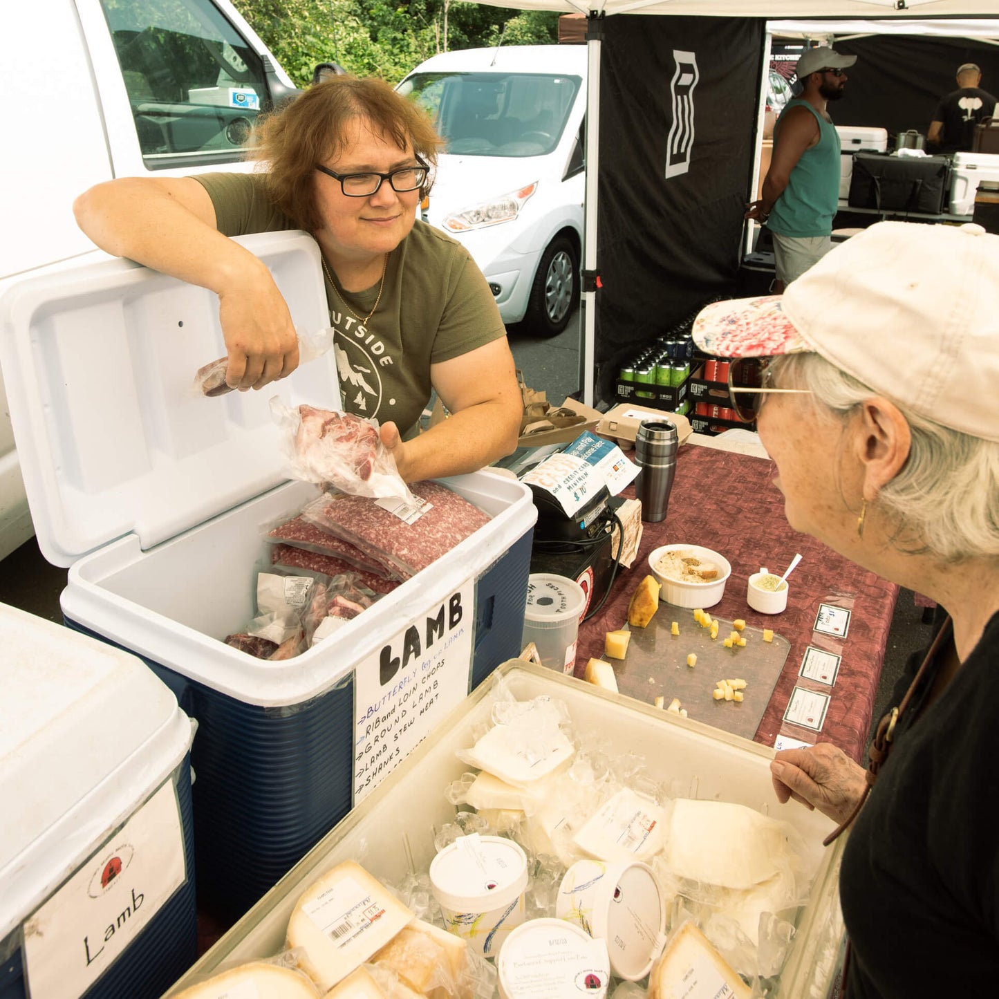 Two women at a vendor tent displaying meats and cheeses