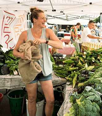 Women at Westport Farmers' Market with sack selling corn smiling