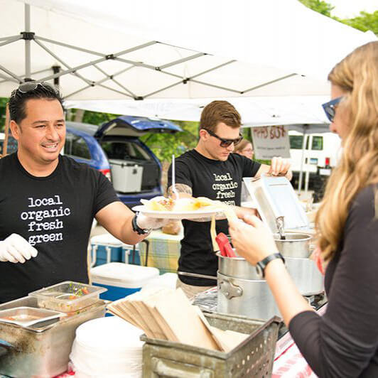 man handing food to person. shirt says organic fresh green