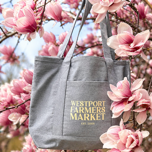 Gray bag with test Westport Farmers Market EST 2006 text on the side. bag is gray. Pink flowers around in background
